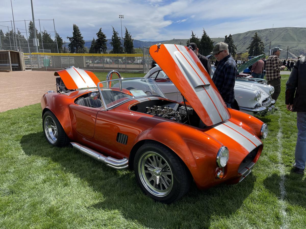 Newer, orange sports car convertible with 2 white racing stripes down the hood.