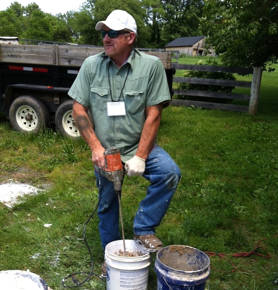 Instructor Allen Cochran is standing behind a 5-gallon bucket. He is holding a drill with a blender attachment mixing mortar